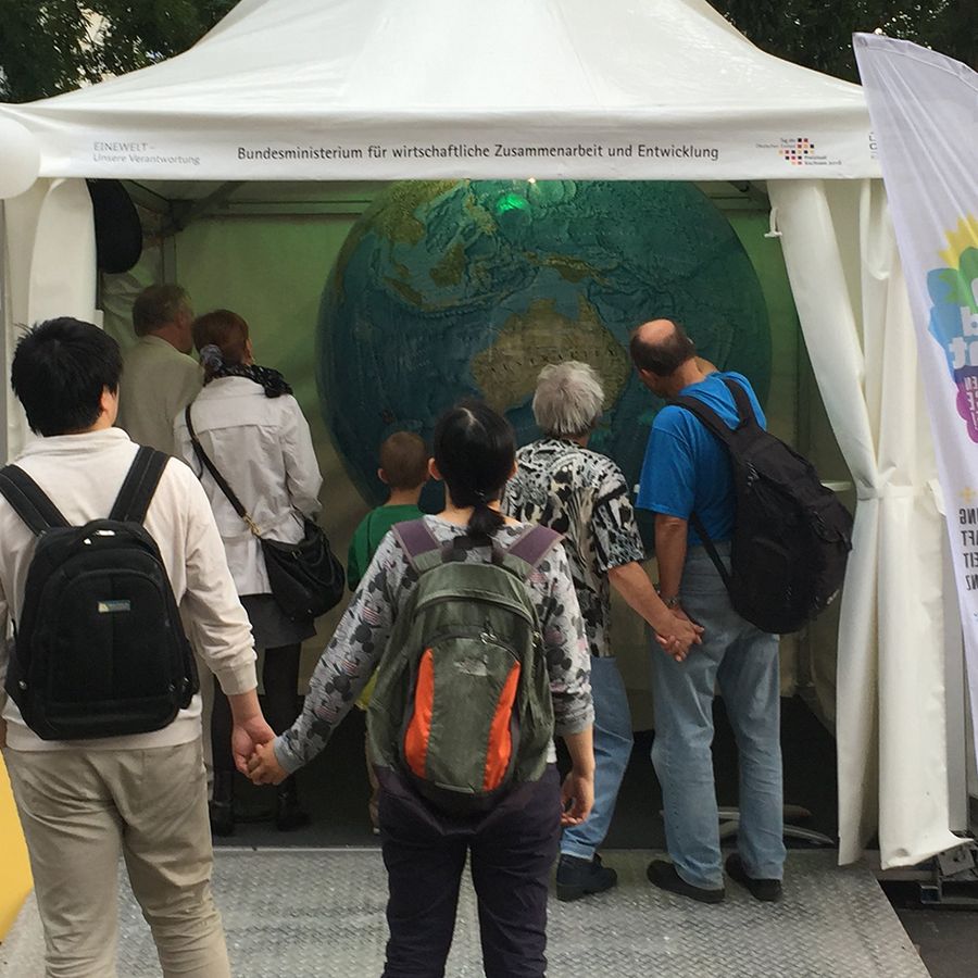 Personengruppe vor einem Zeltstand mit großem Globus. Der Stand trägt die Aufschrift „Bundesministerium für wirtschaftliche Zusammenarbeit und Entwicklung“.