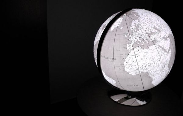 Monochromer Globus auf Metallständer, zeigt Europa, Afrika und Nahost. Weißes Licht hebt geografische Details vor dunklem Hintergrund hervor.