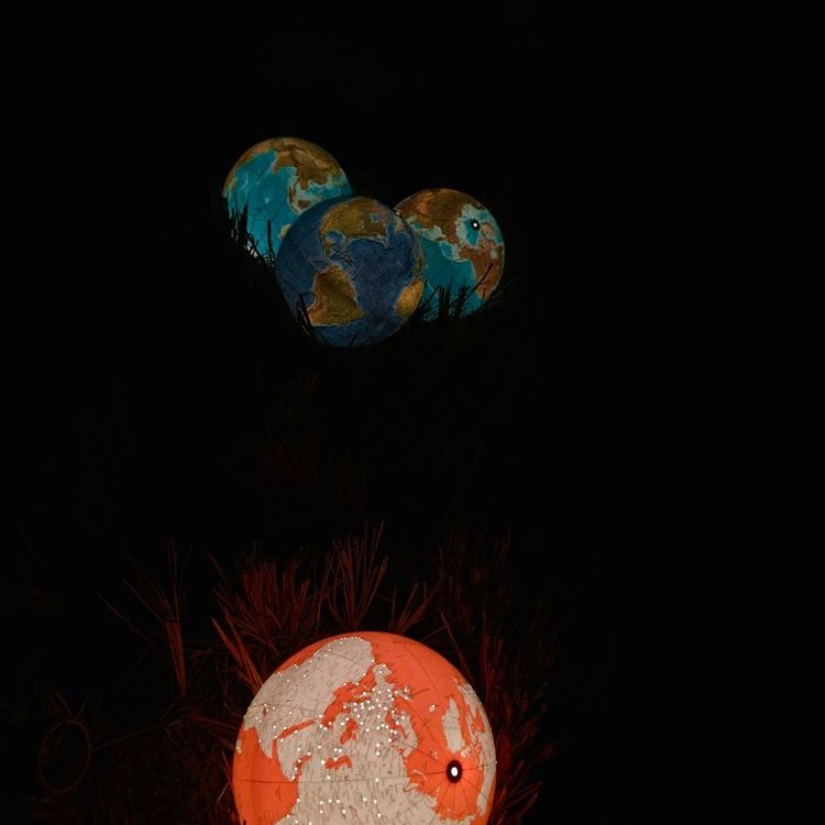 Beleuchteter Globus bei Nacht zwischen Gras, zeigt Amerika. Warme Lichttöne auf Landmassen, kühle Blautöne auf Ozeanen.