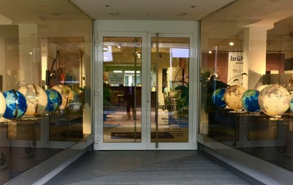 Eingangsbereich eines Showrooms mit dem Schriftzug „brüel“ und „Ambienta“. Beidseitig des Weges sind verschiedenfarbige Globen ausgestellt. Im Hintergrund sind Möbel und Dekoration sichtbar.
