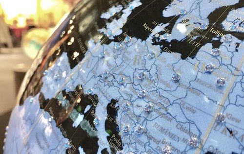 ahaufnahme eines Globus mit Fokus auf Europa. Länder wie Italien, Deutschland und Polen sind sichtbar. Transparente Punkte markieren Städte oder Orte. Der Hintergrund zeigt eine unscharfe Innenraumszene.