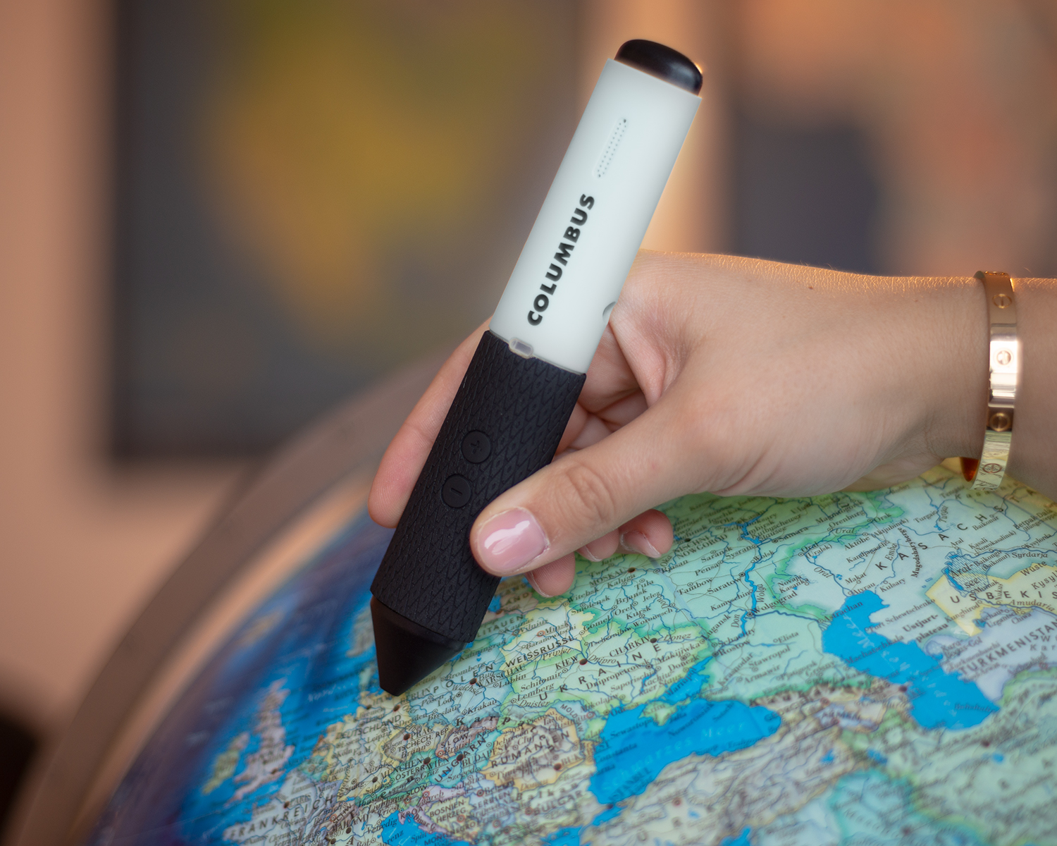 Hand mit Columbus Entdecker-Stift über Globus. Gerät mit zwei Tasten und Markenaufdruck, Globus zeigt geografische Details.
